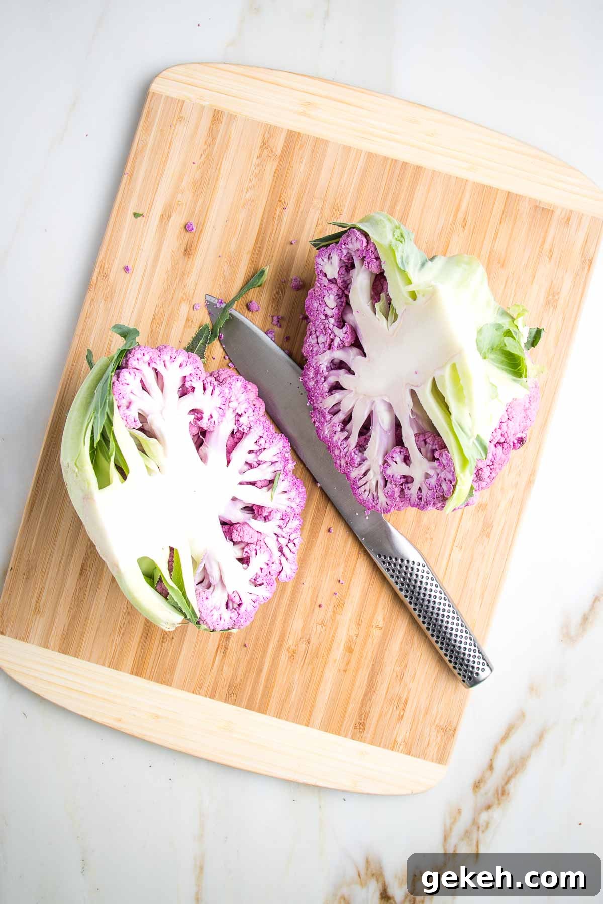 Purple cauliflower cut in half on a wooden board.