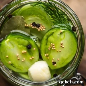 Overhead shot of a jar of pickled sliced green tomatoes and spices on a wooden board.