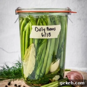 Sealed and labeled jar of dilly beans on a board with dill, peppercorns, mustard seeds, beans and garlic around the base.