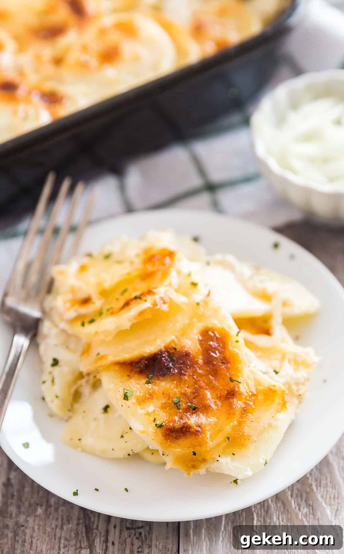 Classic Creamy Scalloped Potatoes Recipe from Mom 2 A plate of scalloped potatoes with a bowl of cheese and the pan of them in the background.