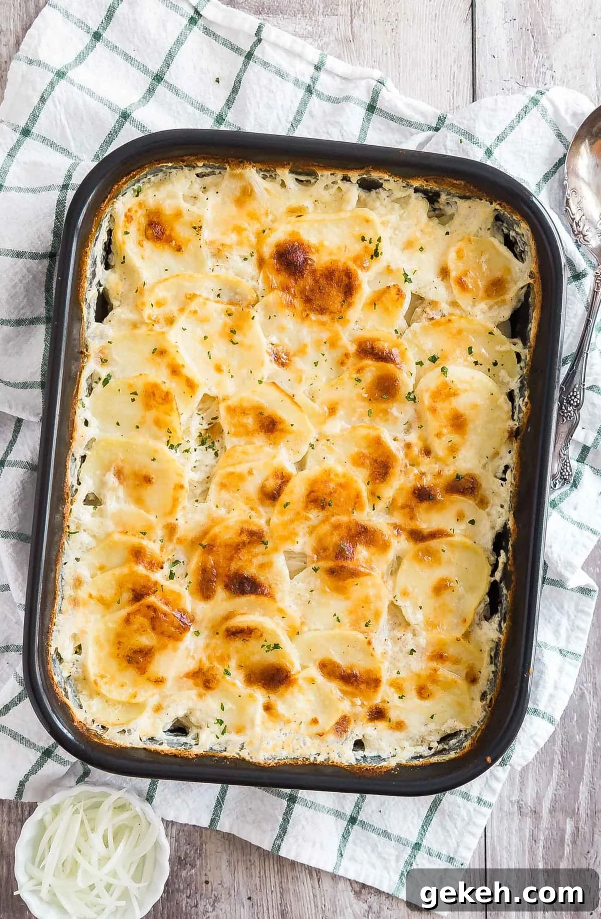 Classic Creamy Scalloped Potatoes Recipe from Mom 3 An overhead image of a pan of scalloped potatoes on a white and black checked towel.