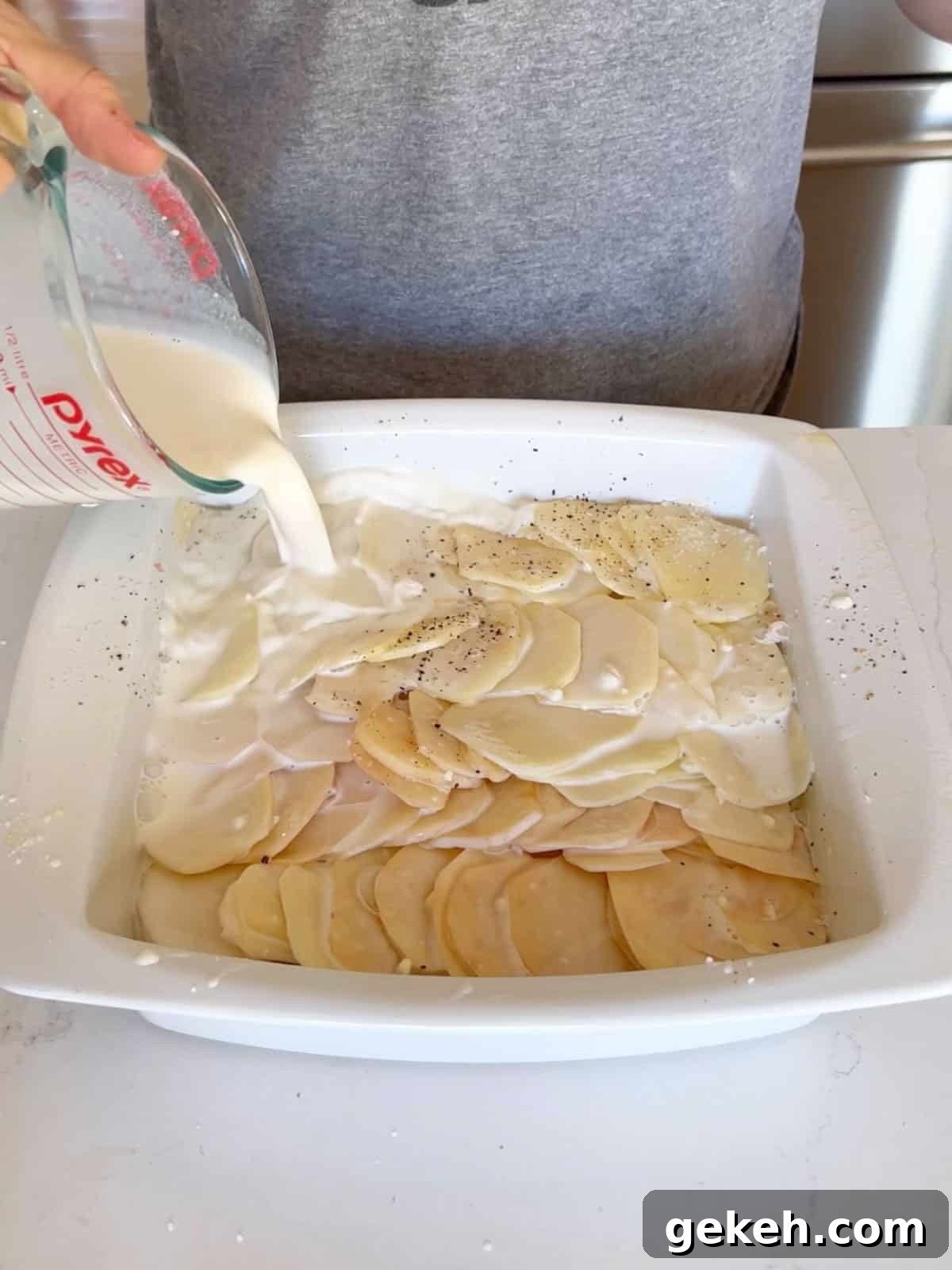 Classic Creamy Scalloped Potatoes Recipe from Mom 7 The milk and flour mixture being poured over the potatoes in the pan.