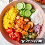 Chicken shawarma in a bowl with turmeric rice, cucumbers, tomatoes, pickles, onions and yogurt sauce.