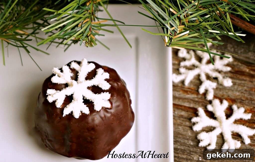 A white plate holding a small cake bundtlette frosted with chocolate ganache and topped with a sugar snowflake.