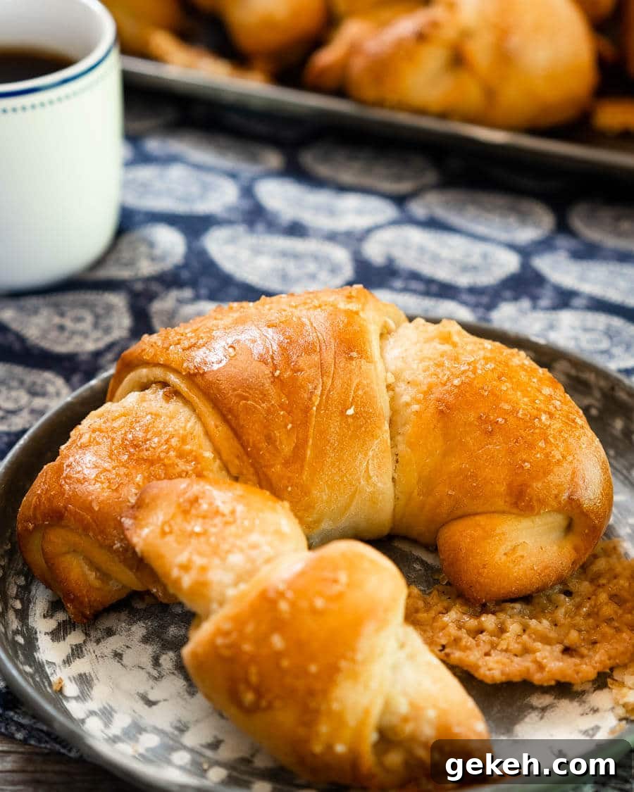 Authentic Kifli (Hungarian Walnut Roll) Recipe for Homemade Pastry 6 A close up of a large Kifli Walnut roll sitting on a metal plate in front of a tray of Kifli Walnut rolls over a blue paisley napkin.