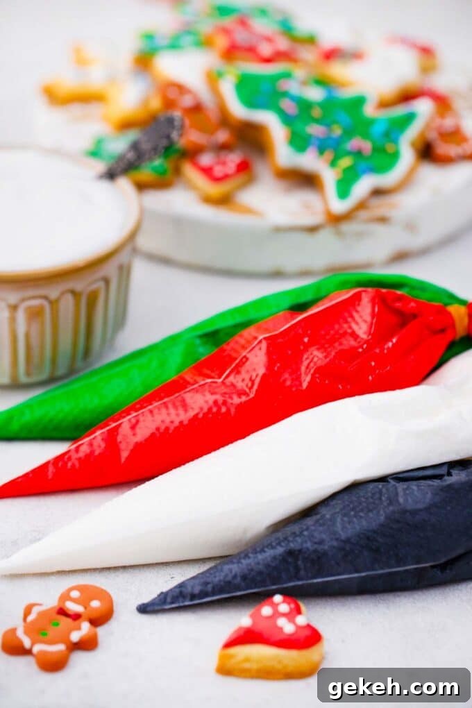 How to Make Smooth Royal Icing for Perfect Cookies and Cakes 2 four piping bags filled with colorful royal icing: greed red white black on a table with cookies in the background