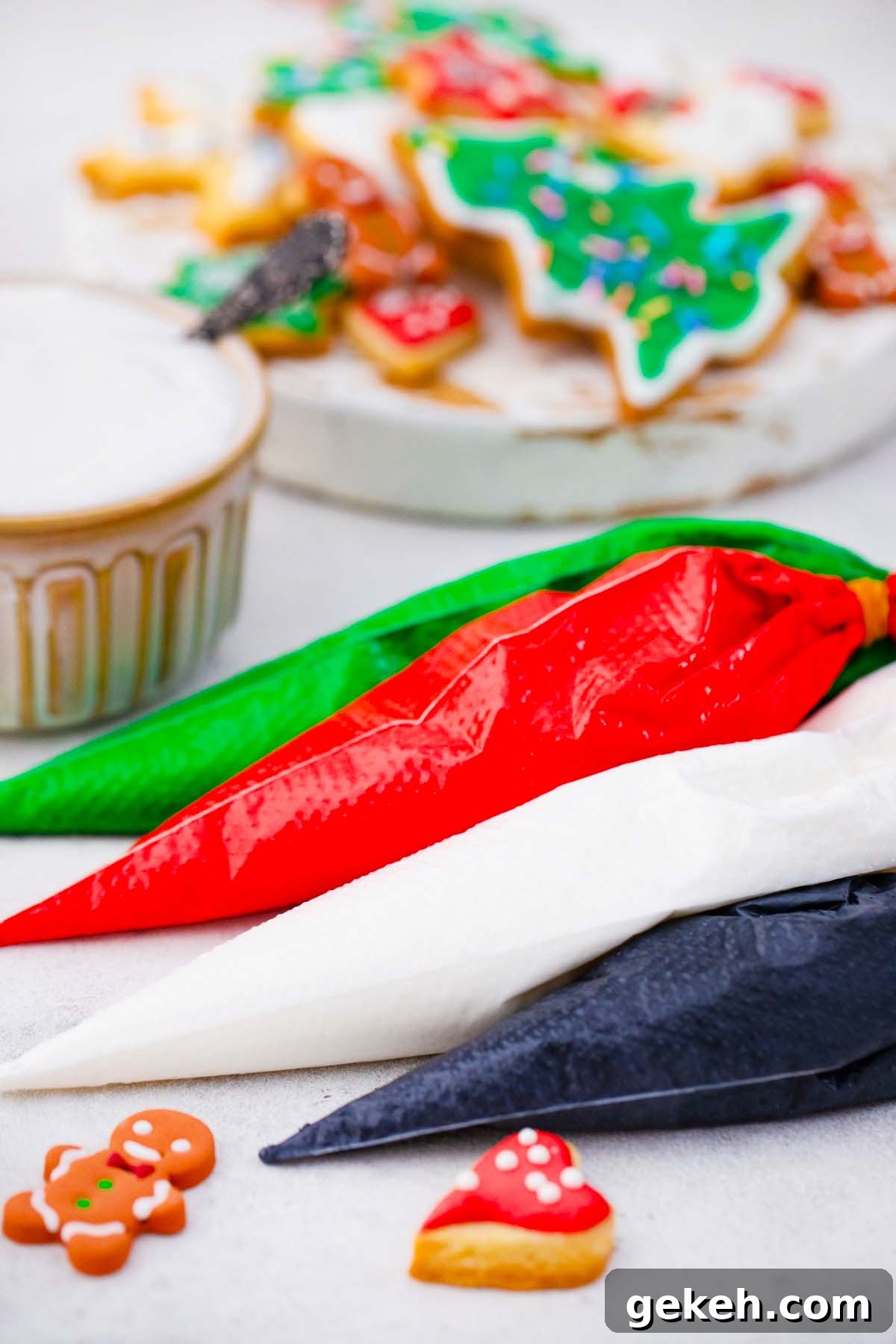 How to Make Smooth Royal Icing for Perfect Cookies and Cakes 15 four piping bags filled with colorful royal icing: greed red white black on a table with cookies in the background