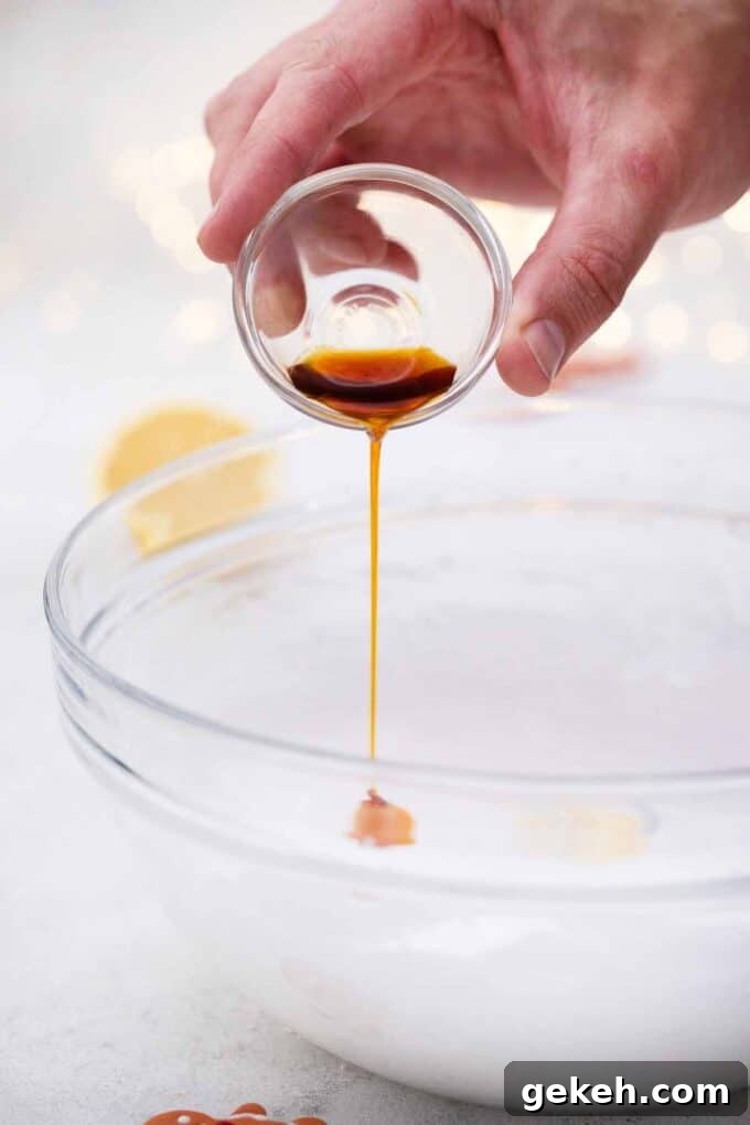 How to Make Smooth Royal Icing for Perfect Cookies and Cakes 5 pouring vanilla extract into a bowl with fluffy egg whites
