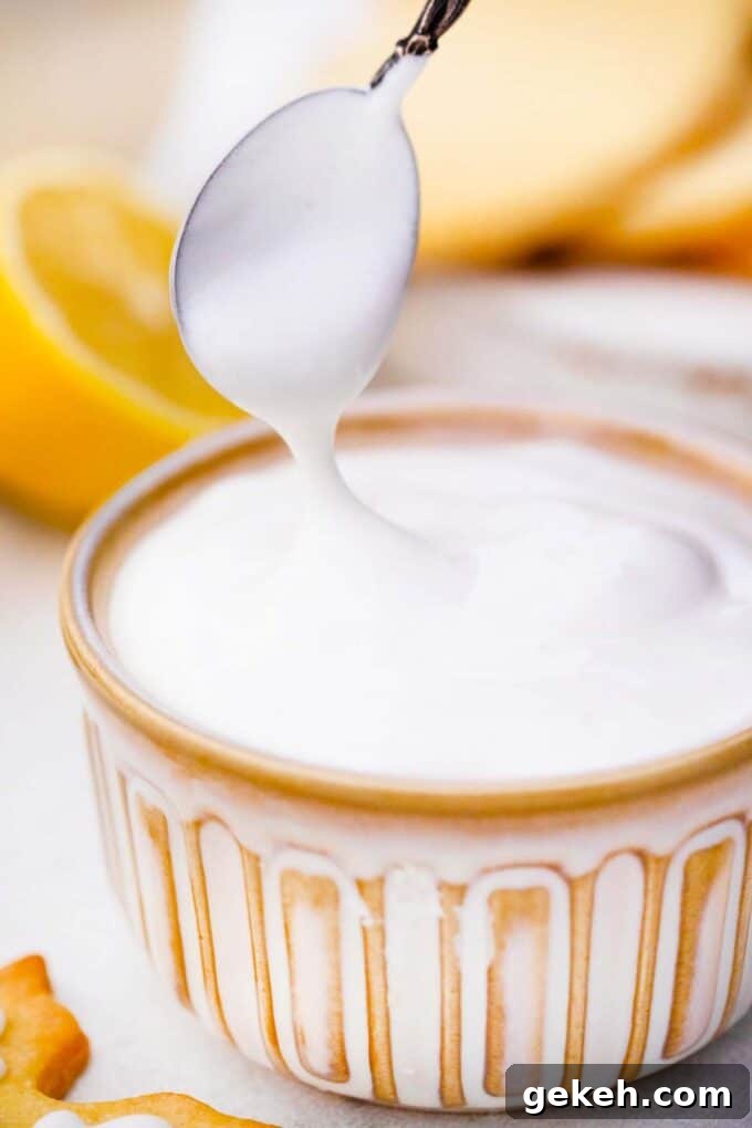 How to Make Smooth Royal Icing for Perfect Cookies and Cakes 7 holding a spoon over white royal icing in a small bowl