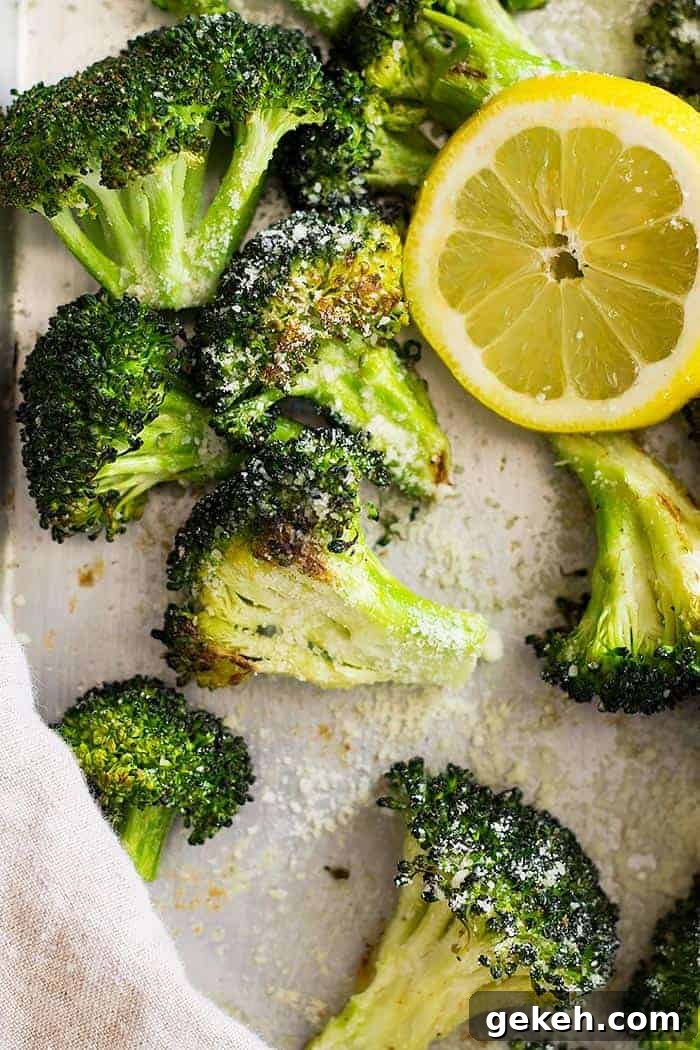 Lemon Parmesan Roasted Broccoli Recipe 2 Close up of lemon parmesan roasted broccoli on a sheet pan with a slice of lemon.