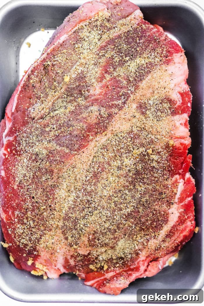 Smoked Chuck Roast Recipe: Tender, Juicy BBQ Roast 3 Raw seasoned beef brisket in a metal baking pan, coated with pepper and spices, ready for cooking—perfect for those who love the flavors of a classic smoked chuck roast.