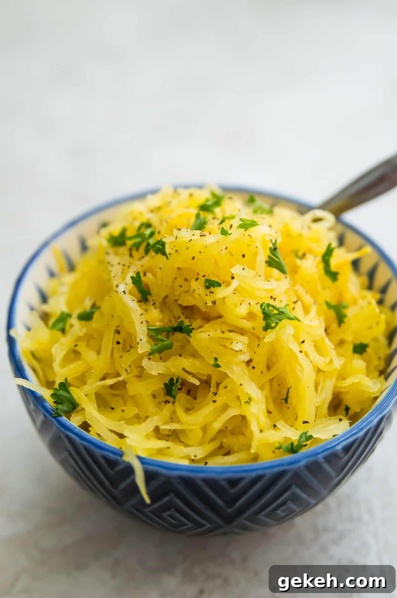 A bowl of cooked spaghetti squash garnished with ground black pepper and fresh parsley.