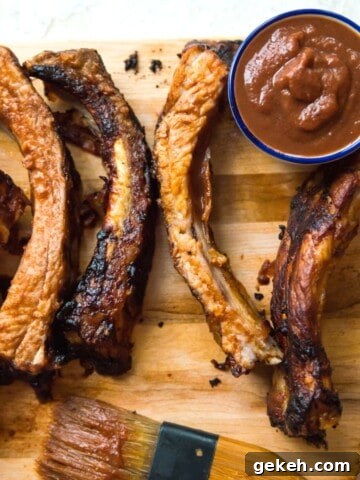 Cooked pork ribs on a serving tray with a side of bbq sauce.