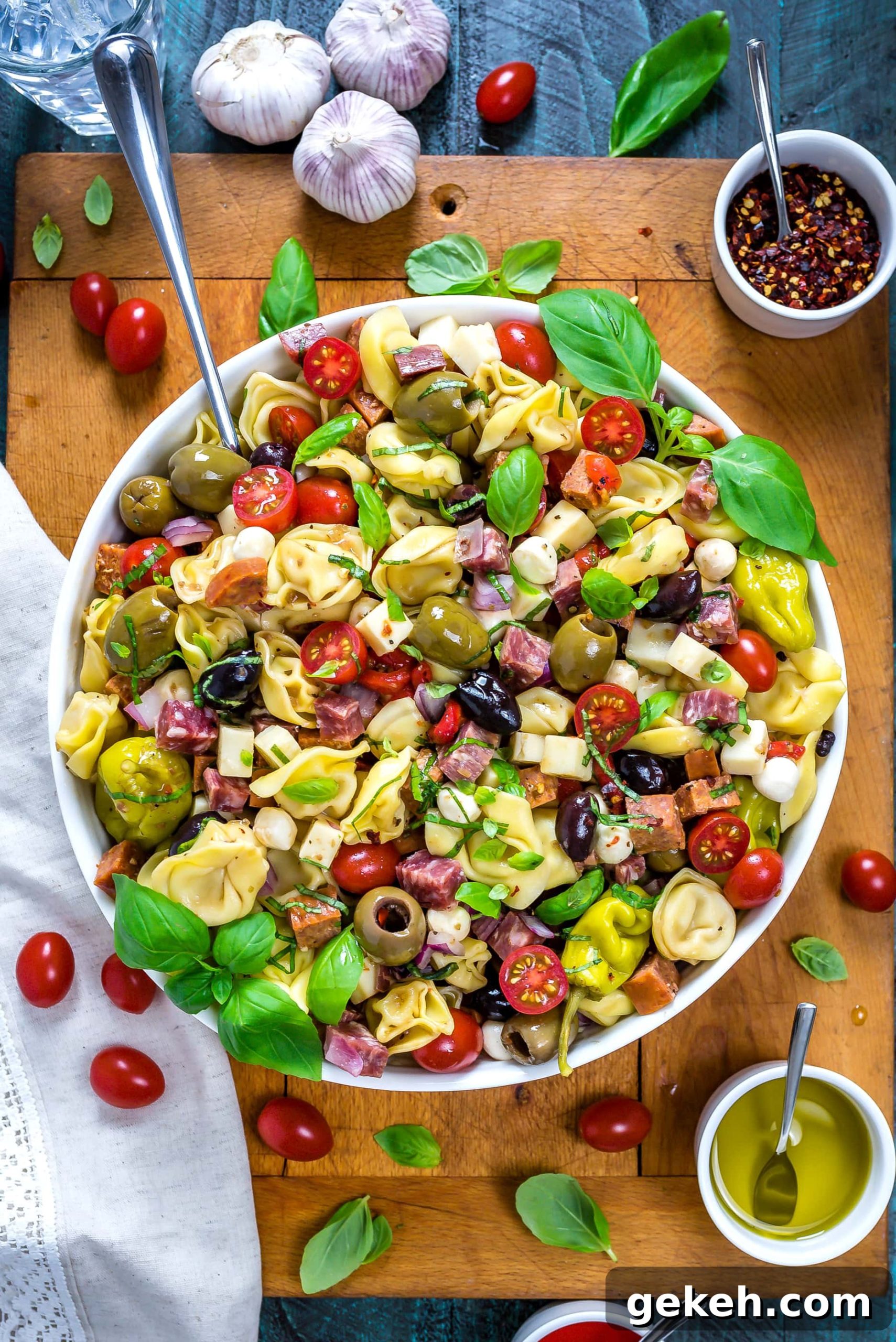 Overhead view of Antipasto Tortellini Pasta Salad in a large white bowl with a large serving spoon.