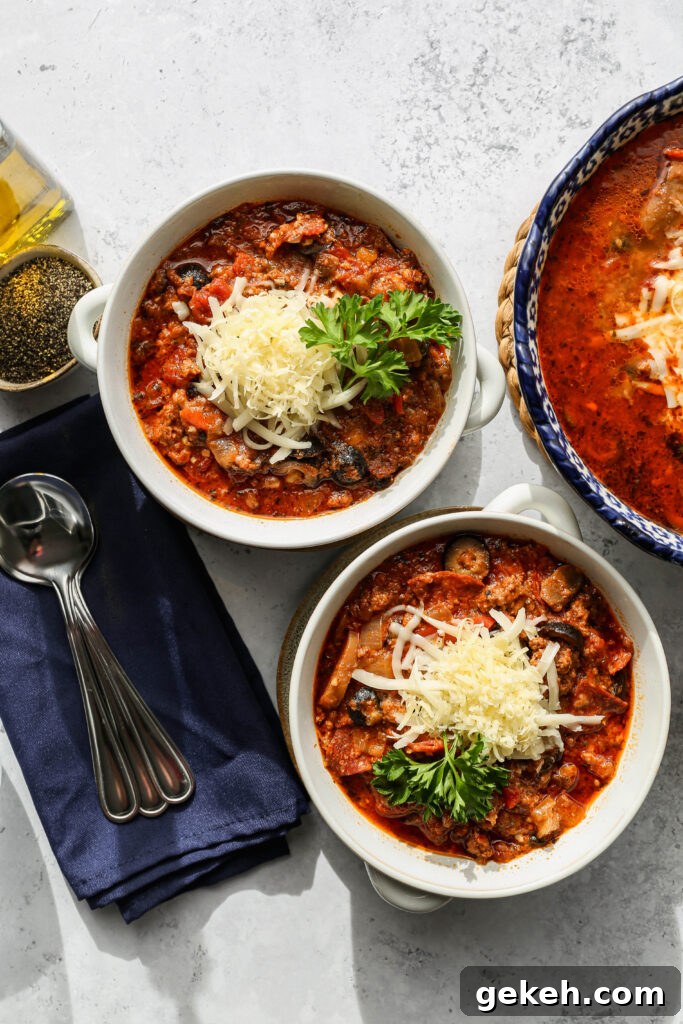 two white bowls of gluten free instant pot pizza soup next to a large blue bowl of soup and a small bowl of pepper.