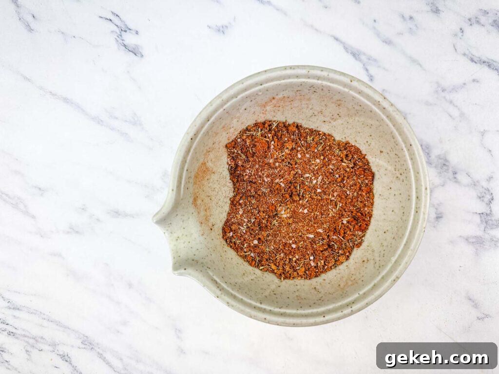 A white bowl containing a blend of various ground spices sits on a white marble surface.