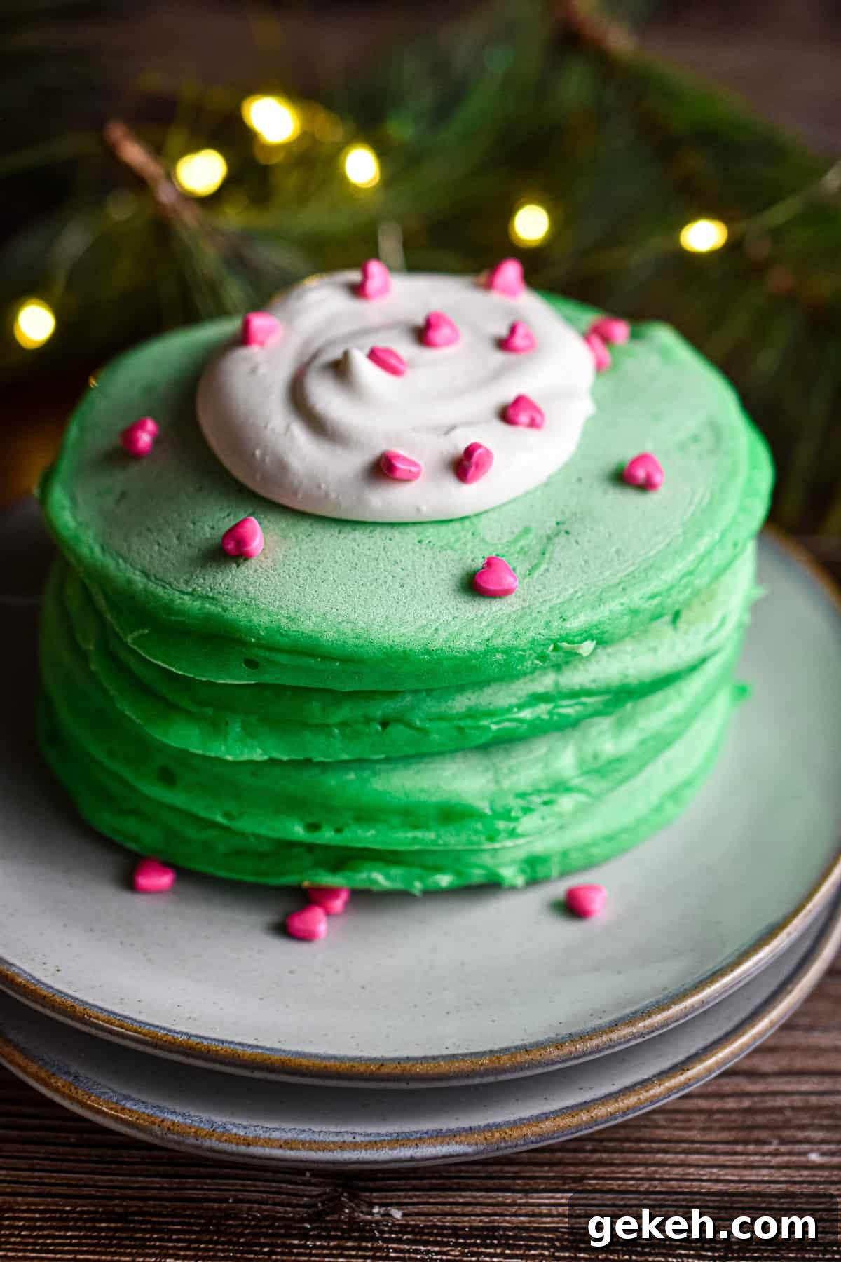 Homemade Grinch Pancakes Recipe — Green St. Patrick’s Breakfast 2 A stack of pancakes has a dollop of whipped cream with heart sprinkles on it.