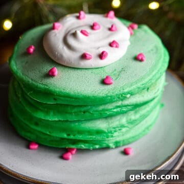 Homemade Grinch Pancakes Recipe — Green St. Patrick’s Breakfast 12 A stack of pancakes has a dollop of whipped cream with heart sprinkles on it.