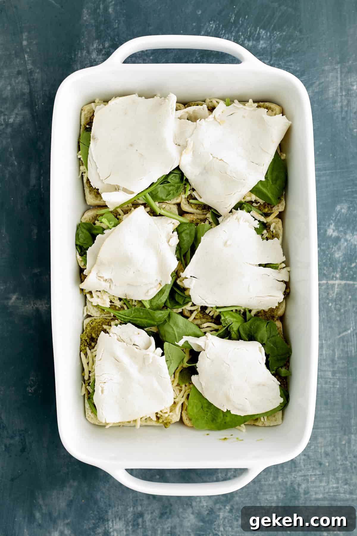 Turkey Caprese Sandwich with Fresh Mozzarella & Basil 6 sliced ciabatta buns in a white baking dish layered with pesto, spinach, and turkey.