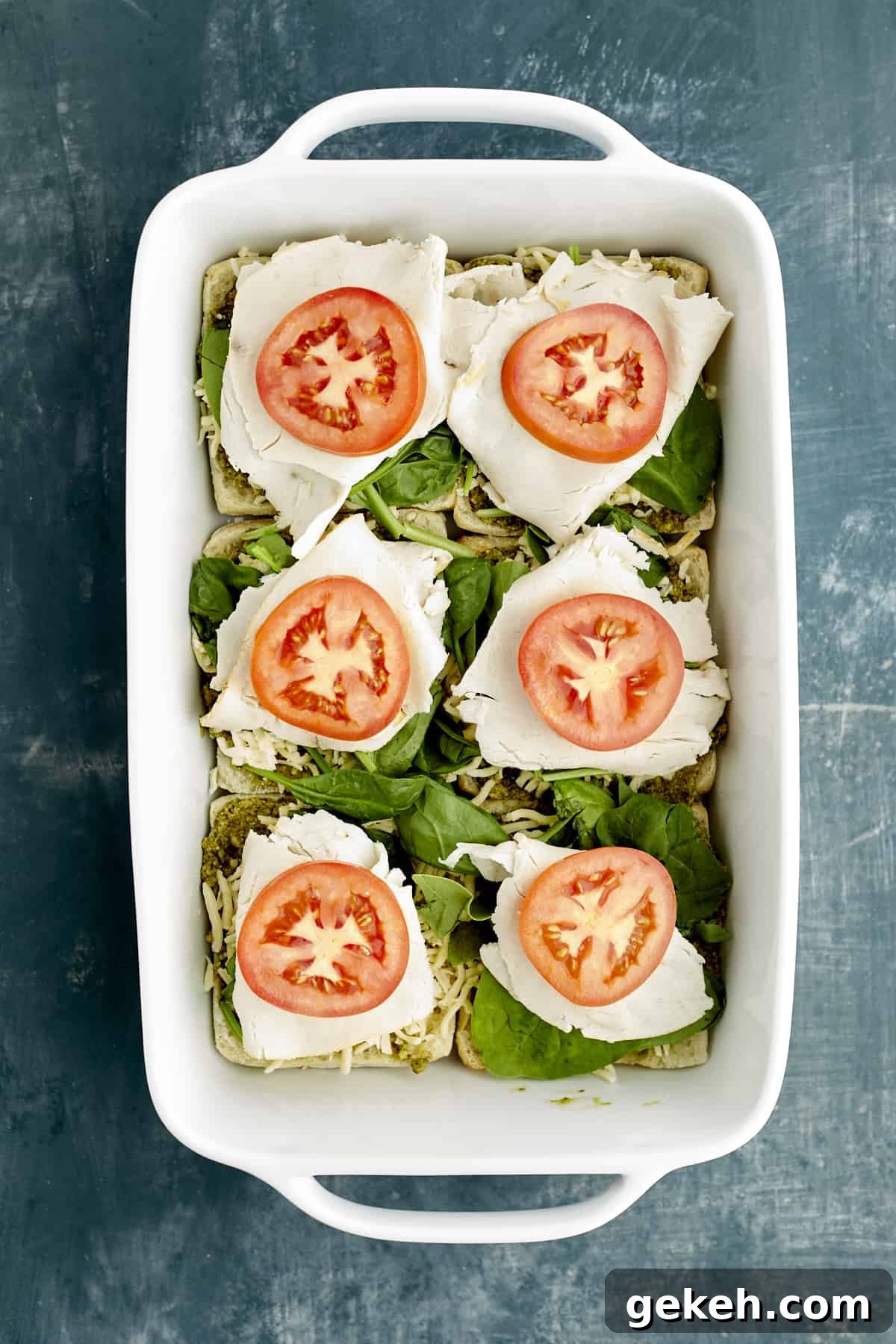 Turkey Caprese Sandwich with Fresh Mozzarella & Basil 7 Sliced ciabatta buns in a white baking dish layered with pesto, spinach, turkey, and tomatoes.