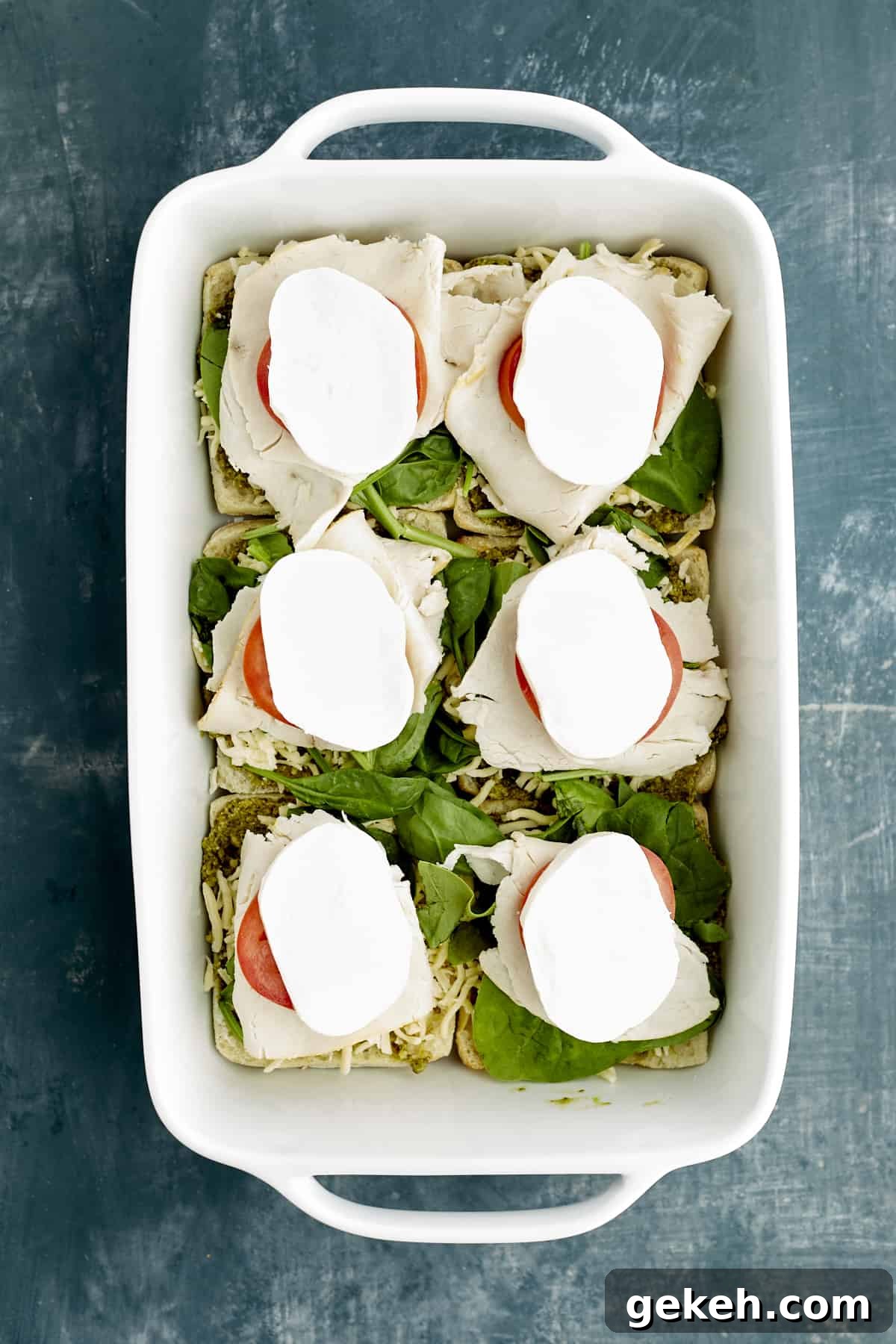 Turkey Caprese Sandwich with Fresh Mozzarella & Basil 8 sliced ciabatta buns in a baking dish layered with pesto, spinach, tomatoes, turkey, and mozzarella.