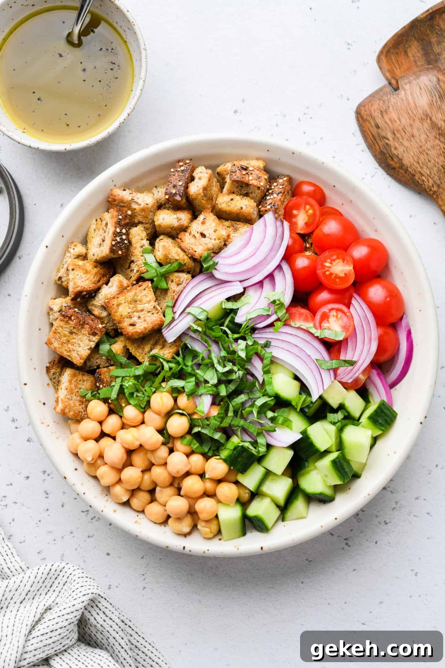 This panzanella salad pairs crispy bread with chickpeas, crunchy veggies, and balsamic vinaigrette. A summer salad that eats like a meal! Overhead view of panzanella salad ingredients combined in a bowl.