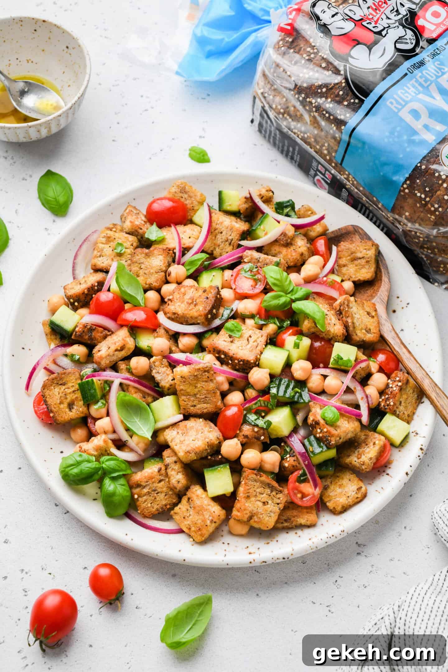 This panzanella salad pairs crispy bread with chickpeas, crunchy veggies, and balsamic vinaigrette. A summer salad that eats like a meal! Overhead view of chickpea panzanella salad on platter with bread in the background