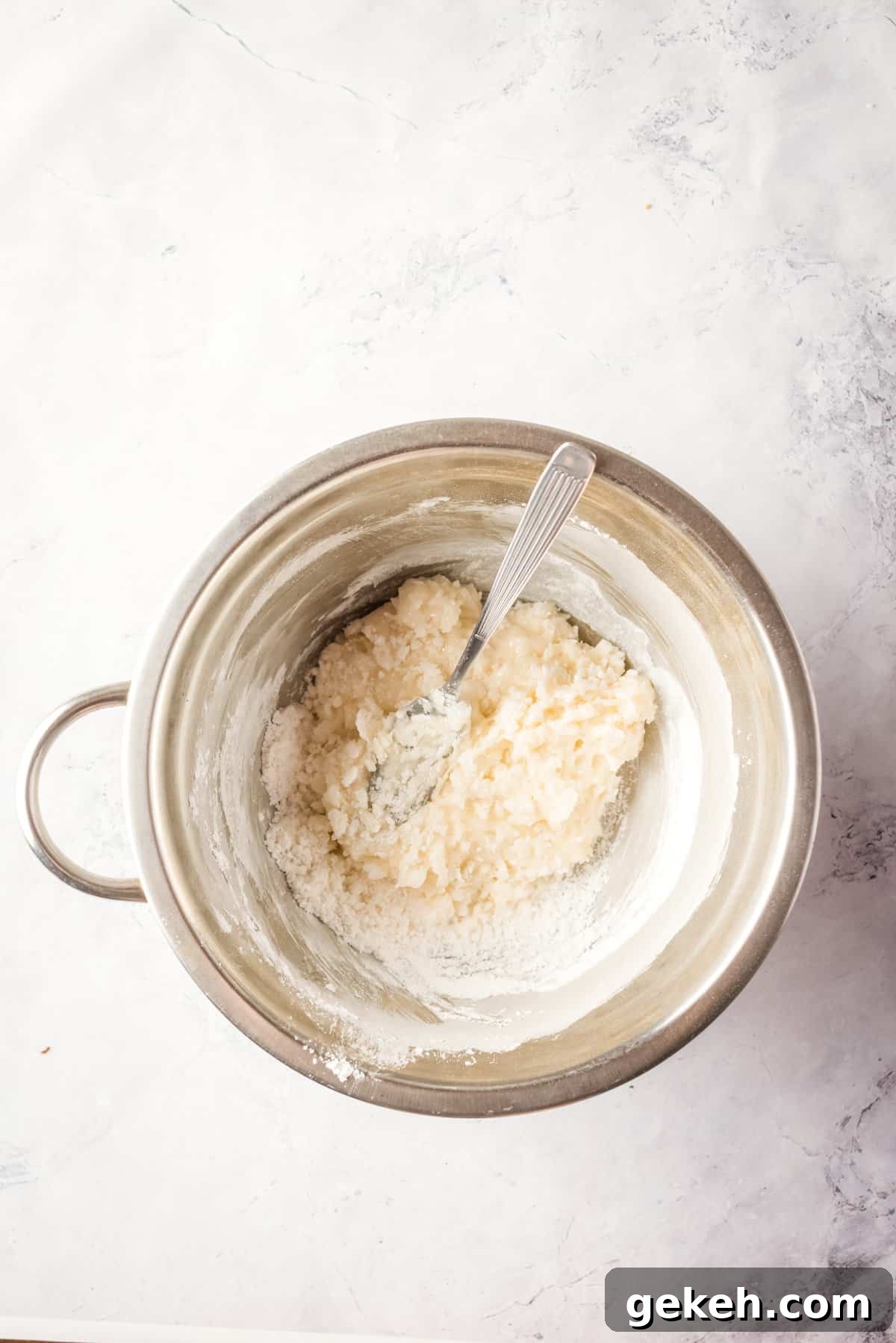 Overhead view showing partially mixed icing mixture in large mixing bowl.