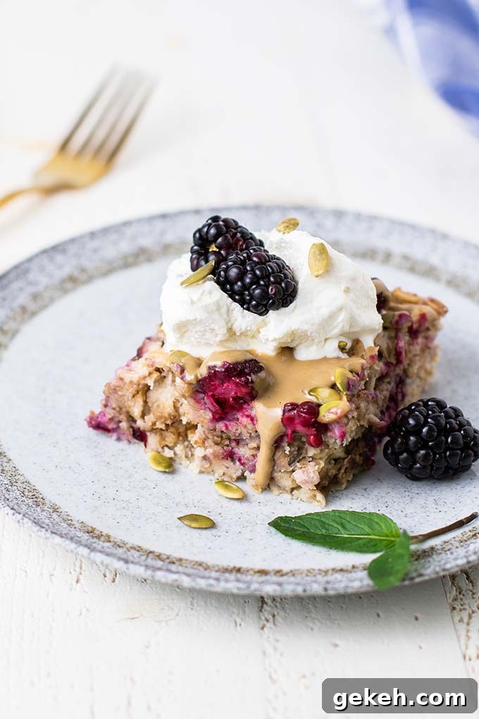 A slice of baked oatmeal on a plate topped with whipped cream and more blackberries.