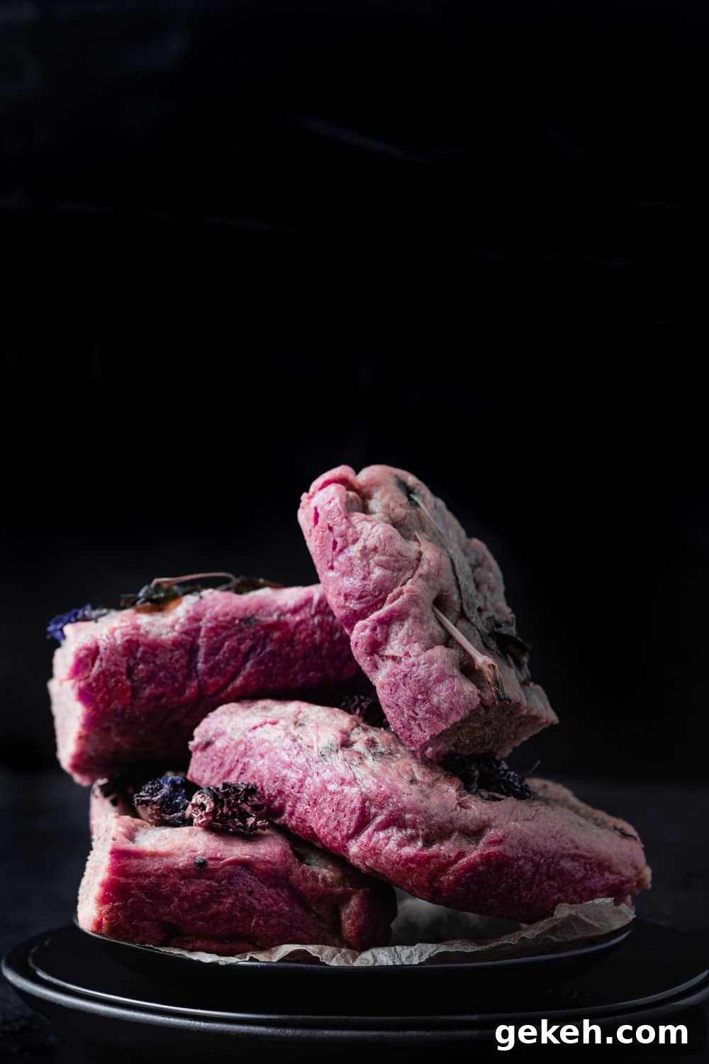 Beet Focaccia: Vibrant No-Knead Magenta Bread Recipe 11 Beet focaccia cut into squares and served on a black plate; straight on shot with a black background.