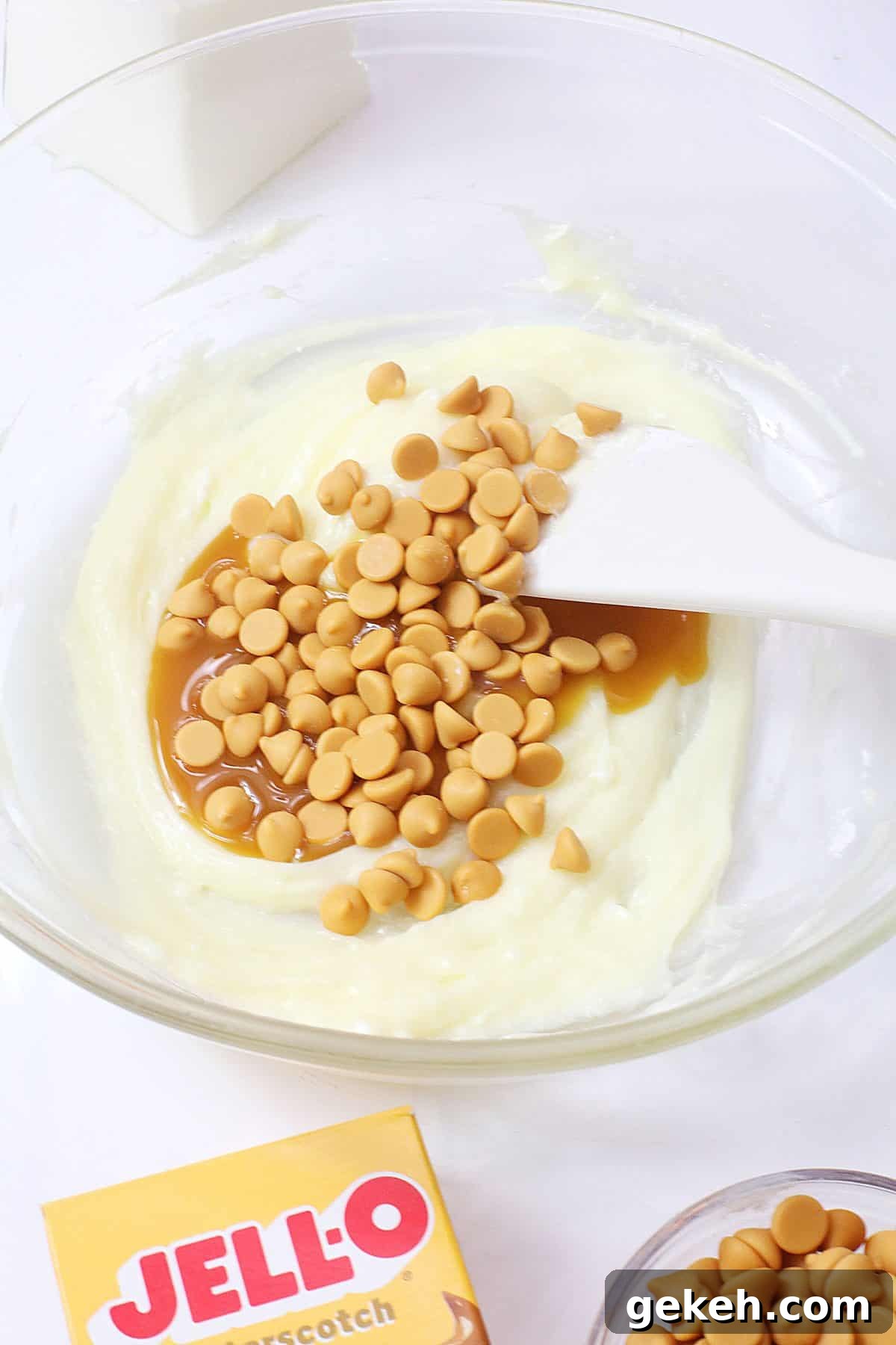 butterscotch chips and butterscotch syrup being folded into cheesecake filling in a glass mixing bowl