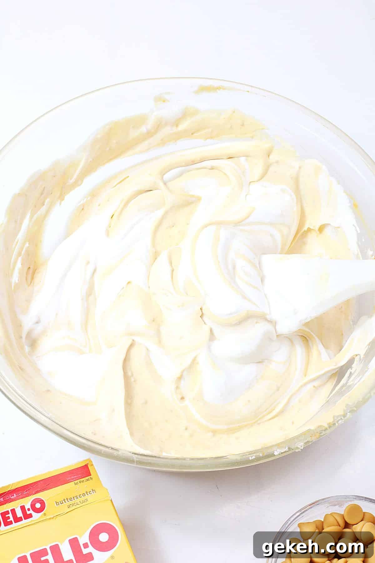 cool whip and butterscotch pudding being mixed together in a glass mixing bowl