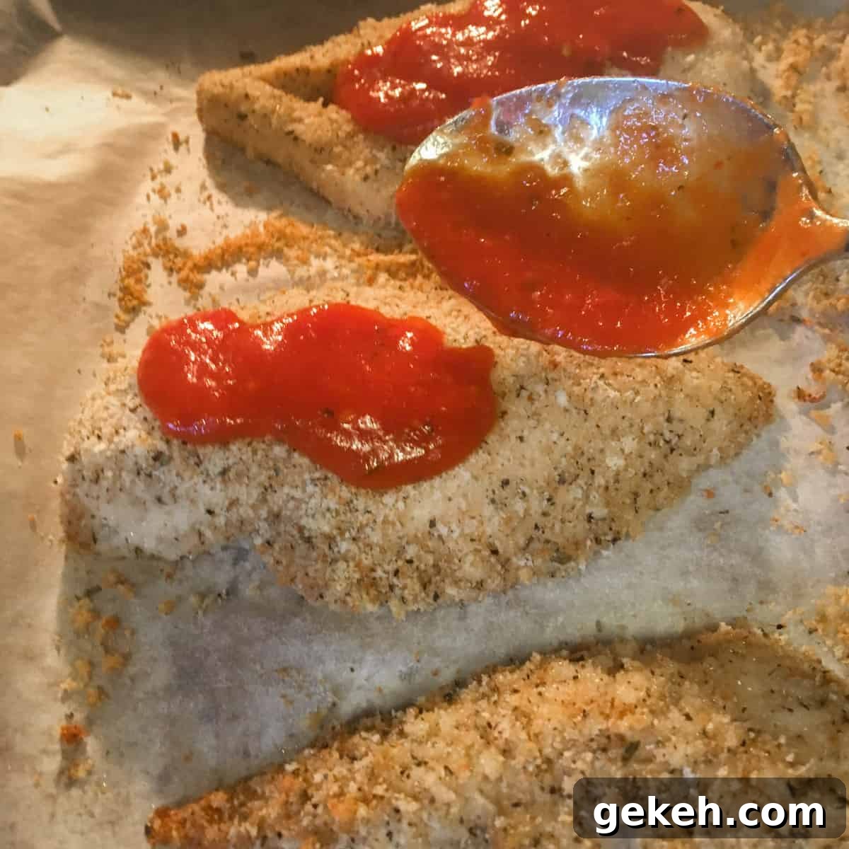 Spooning some pasta sauce on the baked chicken.