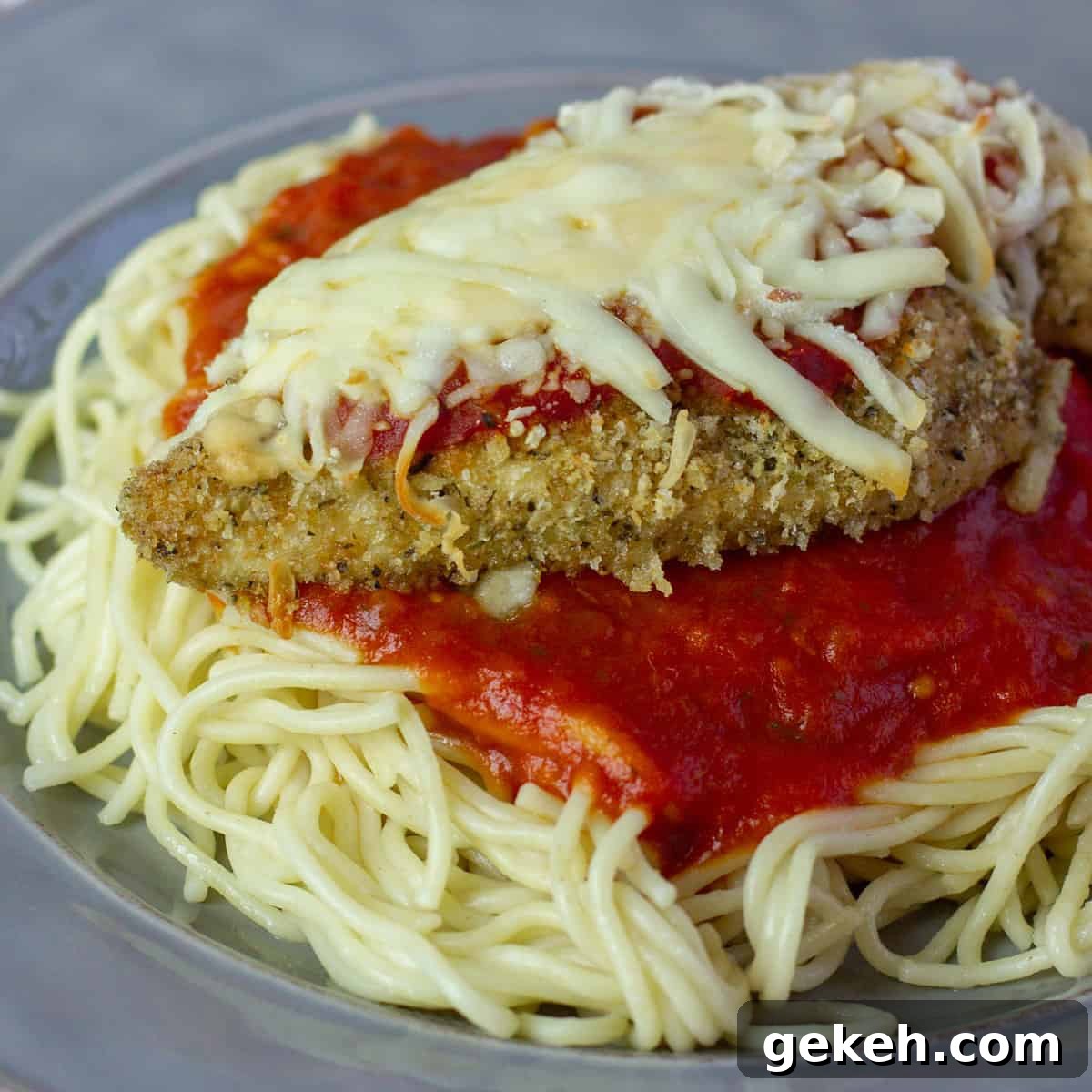 A close up picture of chicken parmesan on spaghetti pasta.