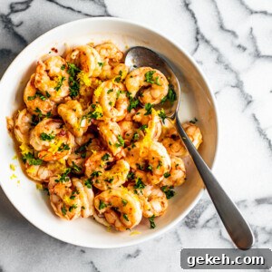 Spicy Lemon Garlic Shrimp with Chilies and Herbs 6 White serving bowl full of buttery shrimp garnished with fresh parsley.
