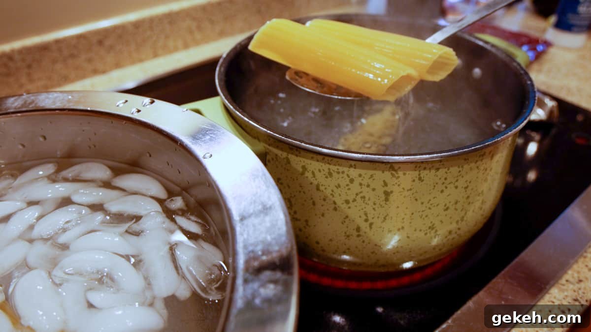 Spooning out of boiling water two manicotti shells with a bowl of ice water next to boiling pot.