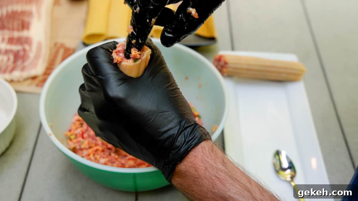Stuffing meat mixture into manicotti shells by hand while wearing black gloves.