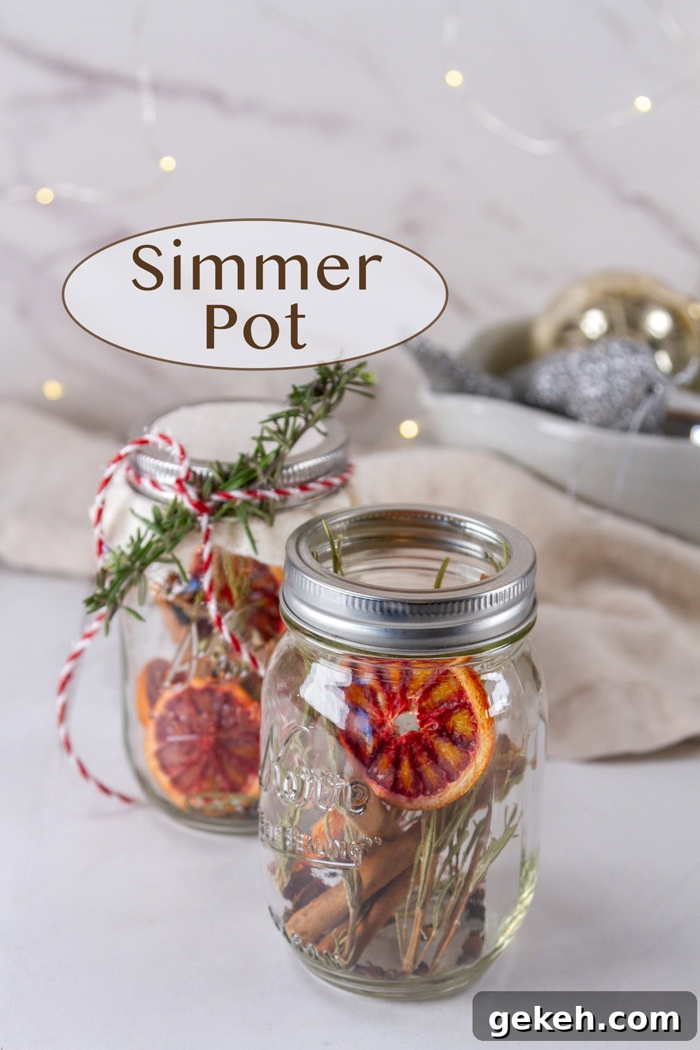 two mason jars filled with simmer pot ingredients in front of twinkle lights and a bowl of Christmas decor.