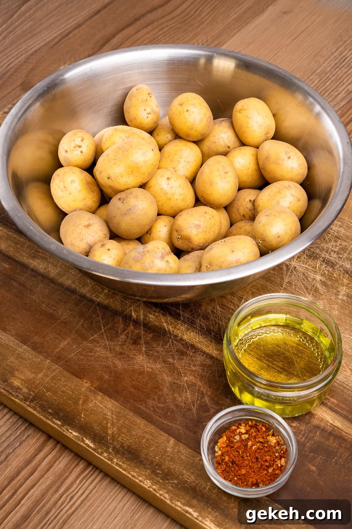 Crispy Air-Fried Baby Potatoes Recipe 11 A bowl of baby potatoes, two glass tumblers filled with olive oil and piri piri seasoning on a wooden chopping board