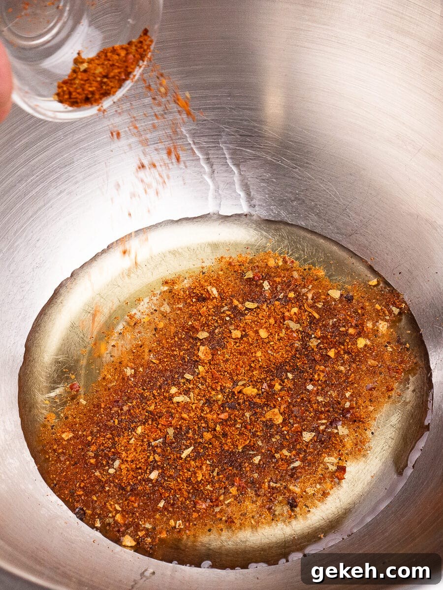 Crispy Air-Fried Baby Potatoes Recipe 14 Pouring piri piri seasoning on top of the olive oil in a large silver mixing bowl