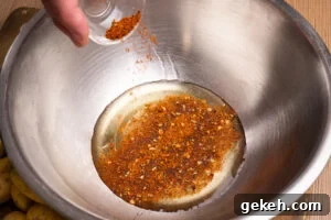 Crispy Air-Fried Baby Potatoes Recipe 6 Pouring piri piri seasoning on top of the olive oil in a large silver mixing bowl