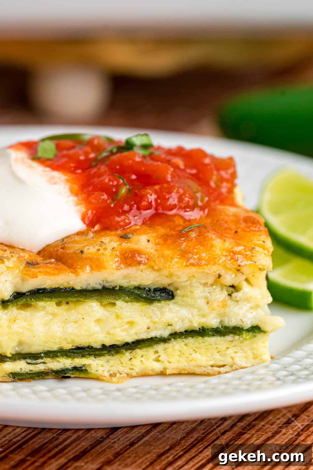 With layers of roasted poblano peppers and gooey cheese topped with fluffy eggs, this Chile Relleno Casserole is easy & flavorful. A slice of chile relleno casserole topped with sour cream and salsa on a white plate