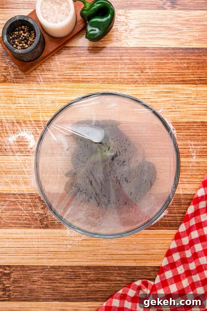 With layers of roasted poblano peppers and gooey cheese topped with fluffy eggs, this Chile Relleno Casserole is easy & flavorful. Poblano peppers in a bowl covered with plastic wrap
