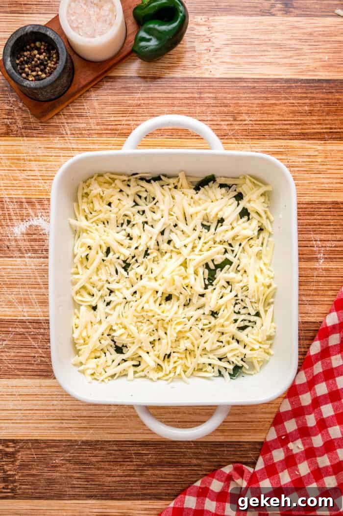 With layers of roasted poblano peppers and gooey cheese topped with fluffy eggs, this Chile Relleno Casserole is easy & flavorful. Shredded cheese on top of poblano peppers in a baking sheet