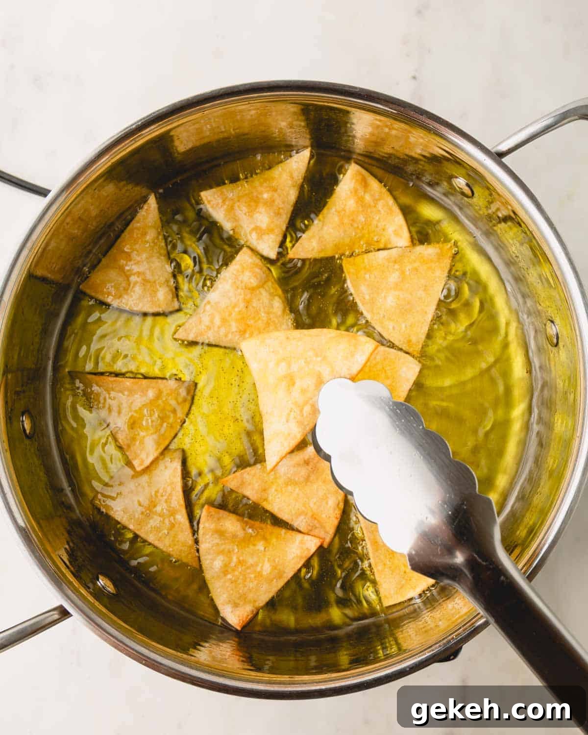 Tongs removing tortilla chips from a pot of oil.