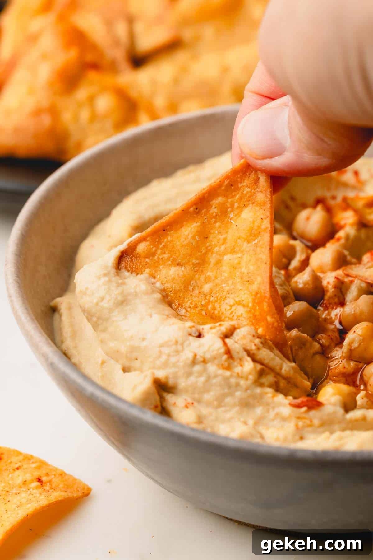 A spicy tortilla chip being dipped into a bowl of hummus.