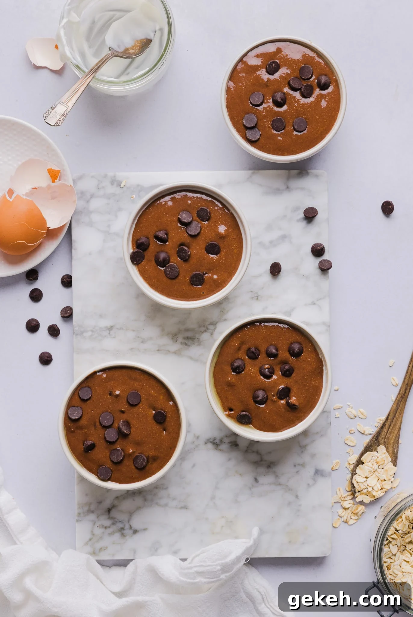 Chocolate baked oats batter poured into ramekins and topped with chocolate chips.