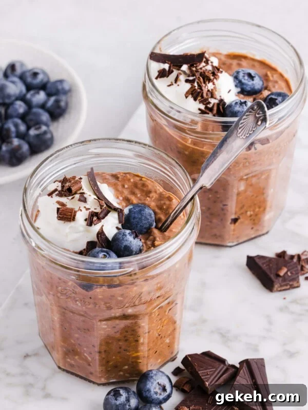 Chocolate protein overnight oats in jars with whipped cream, chocolate shavings and blueberries.