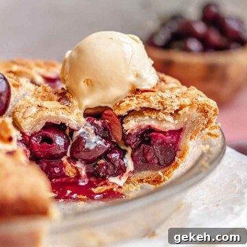 Cherry rhubarb pie slice exposed in a pie pan with ice cream melting on top.