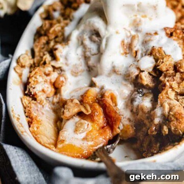 Peach crisp with melted ice cream on top and a serving spoon in the dish.